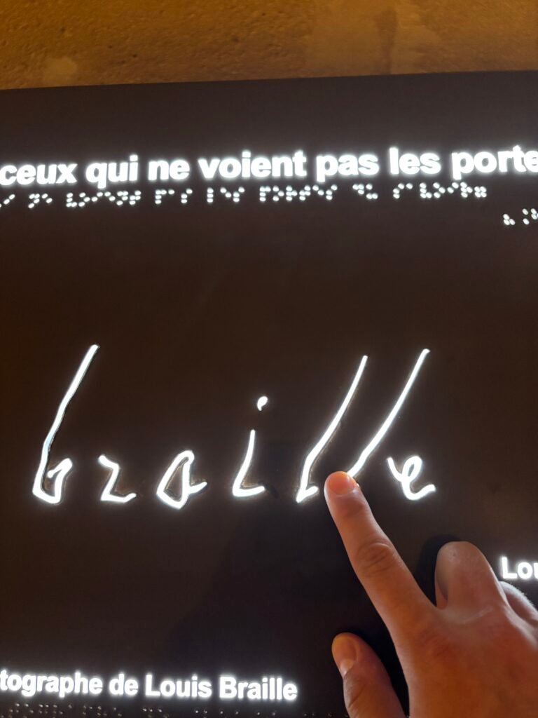 Hand exploring braille letters and tactile signature of Louis Braille, showing link to tactile communication